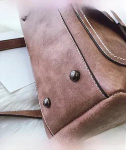 Close-up of vintage brown matte leather bag with bottom metal studs and white stitching