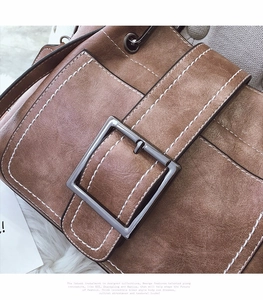 Detail of vintage brown textured leather bag with white stitching and square metal buckle