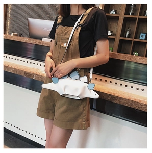 Detailed view of the white and blue dinosaur-shaped crossbody bag worn with a brown outfit