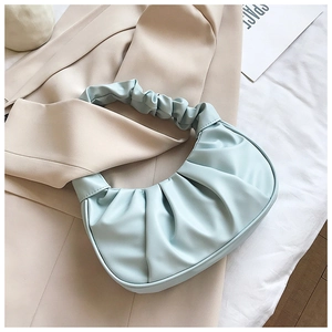 Close-up of pleated mint blue cloud bag detail on beige suit and white fabric background