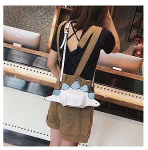 Detail view of a white dinosaur-shaped crossbody bag with blue fins worn by a model
