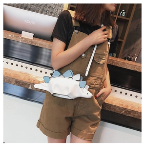 Side view of a creative white dinosaur crossbody bag with blue fins on a female model