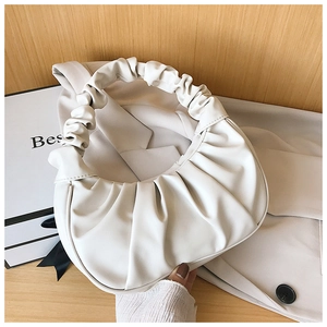 Detail of a creamy white pleated dumpling bag in matte leather on a wooden surface