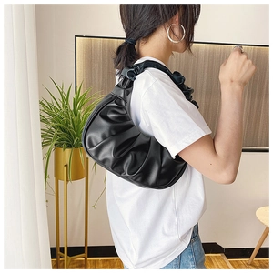 Modern black pleated cloud shoulder bag worn by model in a cozy home interior setting