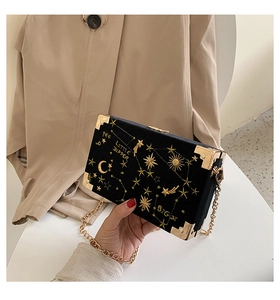 Détail de broderie céleste et coins dorés sur un sac boîte en velours noir