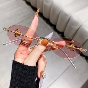Fashionable rimless oval sunglasses with gold bee rhinestone accents and pink tinted lenses