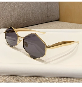 Close-up of golden hexagonal metal sunglasses with dark lenses on a white display tray
