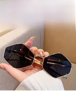 Close-up of golden hexagonal metal sunglasses held by hand with dark grey lenses