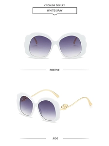Detail view of white scalloped frame sunglasses with gold heart accent and purple lenses