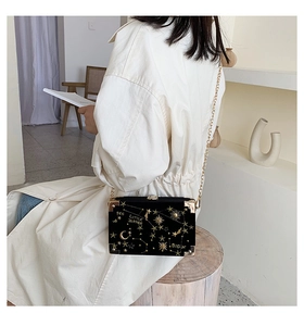 Modèle portant un sac boîte en velours noir avec broderies étoiles dorées et chaîne