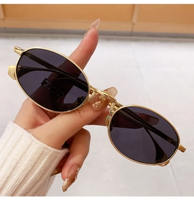 Close-up of golden oval metal sunglasses with purple lenses held in hand for detail