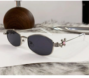 Close-up of silver metal hinge with rhinestone cross and pink gemstone on sunglasses