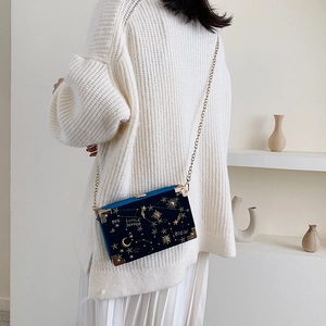 Sac boîte en velours bleu avec broderie étoilée et bandoulière chaîne porté par modèle