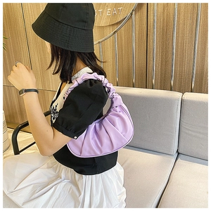 Detail of purple ruched cloud dumpling bag held by a model on a sofa for a French style look