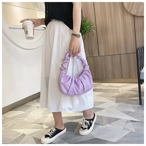 Detail of purple pleated croissant bag with cloud handle worn by a model in outdoor setting