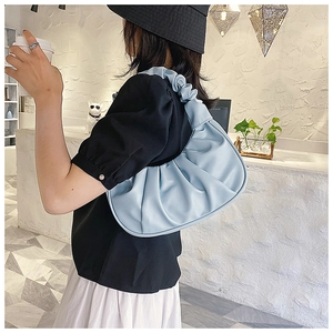 Light blue pleated dumpling bag shown on model in a stylish cafe interior setting