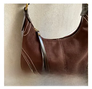 Detailed close-up of dark brown suede shoulder bag showing white stitching and gold hardware