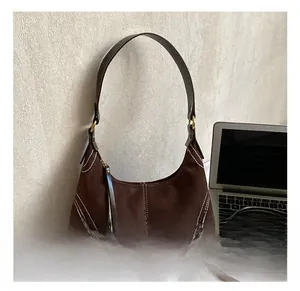 Detail view of brown suede underarm bag with white contrast stitching and long zipper pull