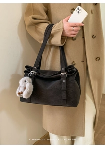 Detail of dark suede tote bag with silver metal buckles and plush rabbit charm