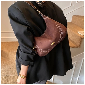 Detail of a brown suede half-moon bag featuring white contrast stitching and a gold nameplate
