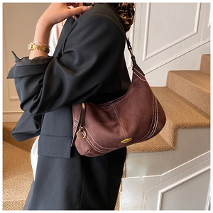 Detail of dark brown suede crescent shoulder bag with white contrast stitching and gold logo