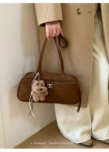 Detalle de bolso hobo de ante marrón oscuro con hebilla plateada y colgante de perro de felpa