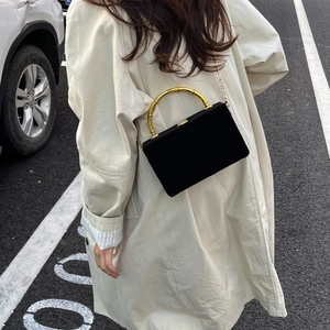 Détail d'un sac en velours noir à poignée en bambou doré porté avec un trench beige