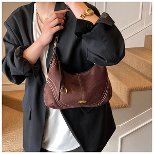 Detail of dark brown suede shoulder bag with white contrast stitching and gold logo plate