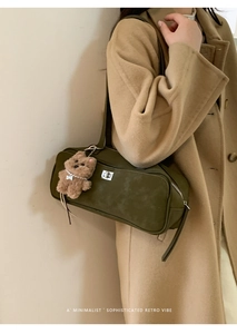 Detalle de bolso bandolera verde oliva con hebilla plateada y accesorio colgante de oso de peluche