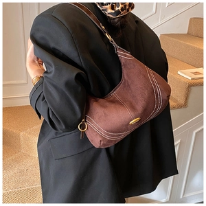 Detail of a brown suede hobo bag with contrast stitching and gold logo plate