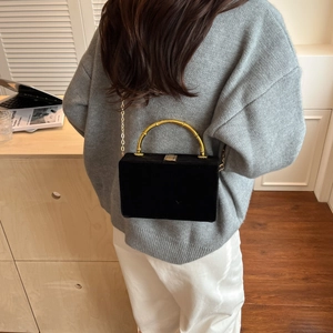 Détail d'un sac à bandoulière en velours noir avec poignée en bambou doré porté par un modèle