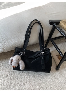 Detailed view of black canvas tote bag with plush bunny charm on minimalist background
