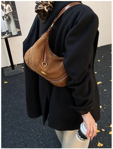 Detail of brown suede hobo bag featuring white contrast stitching and gold buckle hardware