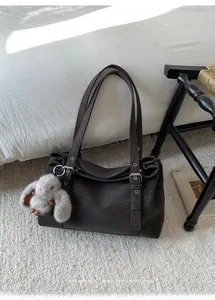 Detail of dark brown tote bag featuring adjustable side straps and gray plush rabbit charm