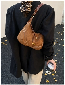 Detail of brown suede hobo bag with contrast stitching and golden metallic hardware