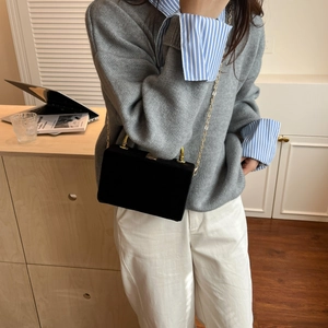 Petit sac en velours noir avec bandoulière en chaîne dorée porté par un mannequin