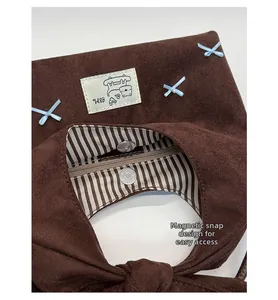 Detail of dark brown suede bag featuring magnetic closure and blue ribbon bow detail