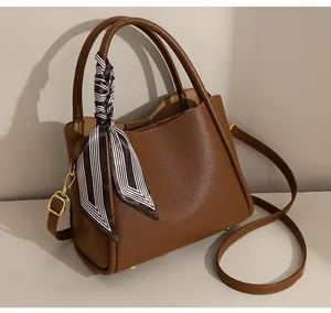 Detail of brown litchi pattern leather handbag with striped scarf and golden buckle