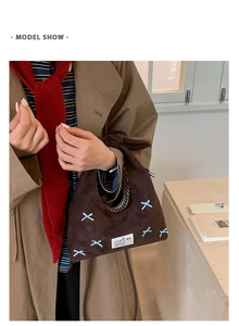 Detailed view of brown suede crossbody bag with blue patterns worn with a trench coat