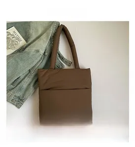 Flat lay of a brown quilted nylon tote bag with long handles and fashion props