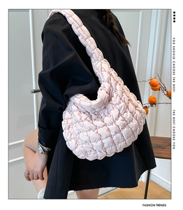 Vista lateral de un bolso nube acolchado rosa con correa ancha para el hombro en una modelo