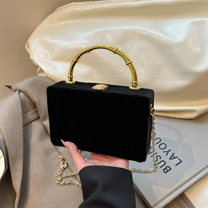 Détail d'un sac boîte en velours noir avec poignée en bambou dorée et bandoulière