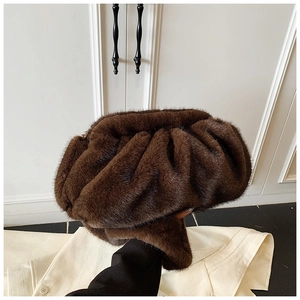 Detail of a dark brown faux fur cloud clutch bag with soft pleated texture held by a model
