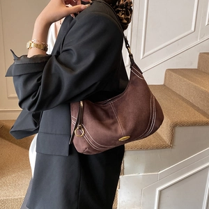 Brown suede shoulder bag with contrast stitching and crescent shape shown on model