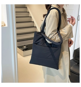 Detail of a black quilted down tote bag with padded handles and soft horizontal texture