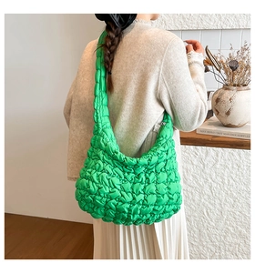 Close-up of bright green puffy quilted shoulder bag with glossy texture and moon shape