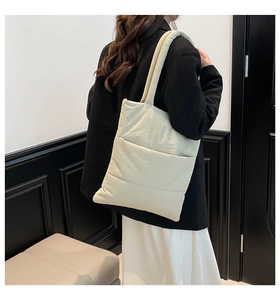 Detail of light beige quilted puffy tote bag with soft padded straps on female model