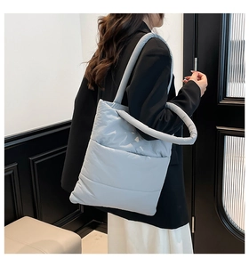 Side view of a light grey-blue quilted down tote bag worn by a model in a minimal room