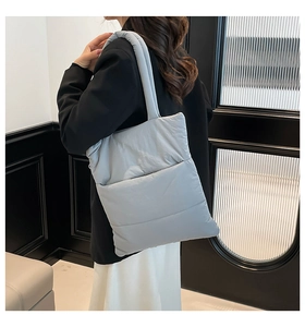 Detail of light blue quilted tote bag with padded shoulder strap shown on model back