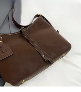 Detail view of brown leather tote featuring white stitching and gold metal bottom studs